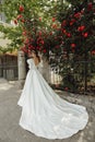 Beautiful bride with blond hair in luxurious wedding dress posing in the spring garden with blooming roses bushes Royalty Free Stock Photo