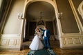 Beautiful bride with bouquet and handsome groom wearing blue suit dancing in arch at yellow walls background