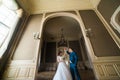 Beautiful bride with bouquet and handsome groom wearing blue suit dancing in arch at yellow walls background