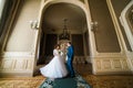 Beautiful bride with bouquet and handsome groom wearing blue suit dancing in arch at yellow walls background