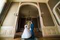 Beautiful bride with bouquet and handsome groom wearing blue suit dancing in arch at yellow walls background