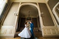 Beautiful bride with bouquet and handsome groom wearing blue suit dancing in arch at yellow walls background