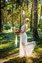 Beautiful bride with a bouquet in her hand posing on her wedding day among the green trees in summer forest. The happy bride smile Royalty Free Stock Photo