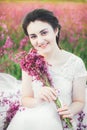 Beautiful bride in a flower field. The girl in a white dress with a bouquet in a summer field at sunset Royalty Free Stock Photo