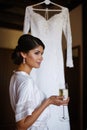 Beautiful bride girl with a glass of champagne in hand near a wedding dress.