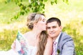 Beautiful bride and groom sitting in grass and kissing. Young wedding couple Royalty Free Stock Photo