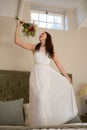 Beautiful bride holding bouquet singing while standing on bed at home Royalty Free Stock Photo