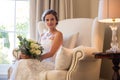 Beautiful bride holding bouquet sitting on armchair at home Royalty Free Stock Photo