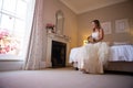 Beautiful bride holding bouquet while sitting on bed at home Royalty Free Stock Photo