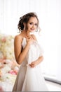 Beautiful bride is holding her wedding dress in the boudoir room. look at the camera