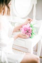 A beautiful bride is holding a peonies in her hands sitting at a white dressing table with a mirror, pearl necklace Royalty Free Stock Photo