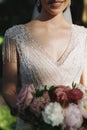Beautiful bride is holding a wedding colorful bouquet in lace dress with beads. Beauty of colored flowers. Close-up. Bridal Royalty Free Stock Photo