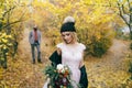 Beautiful bride in a knitted hat with a pompon are posing in autumn forest on blurred groom`s background. Wedding Royalty Free Stock Photo