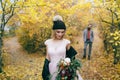 Beautiful bride in a knitted hat with a pompon are posing in autumn forest on blurred groom`s background. Wedding Royalty Free Stock Photo