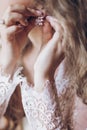 Beautiful bride in lace robe putting on luxury earrings, bridal