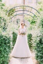 Beautiful bride is looking on the bouquet while standing above the arch.