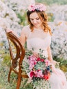 Beautiful bride is looking at the wedding bouquet while sitting on the chair in the mountains.