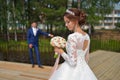 Beautiful bride looking at wedding bouquet, stylish groom waits for her opposite Royalty Free Stock Photo