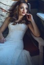 Beautiful bride in luxurious wedding dress with sweetheart neckline sitting ion the vintage sofa in relaxed pose Royalty Free Stock Photo