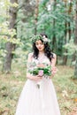Beautiful bride in nature in a coniferous forest in a wreath on her head and a luxurious wedding dress. Rustic boho Royalty Free Stock Photo