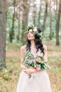 Beautiful bride in nature in a coniferous forest in a wreath on her head and a luxurious wedding dress. Rustic boho Royalty Free Stock Photo