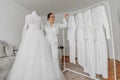 a beautiful bride poses in a white robe next to her wedding dress and her friends' dresses