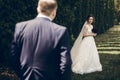 Beautiful bride with red flowers bouquet looking at stylish groom walking towards her, happy newlywed couple posing outdoors near Royalty Free Stock Photo