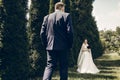 Beautiful bride with red flowers bouquet looking at stylish groom walking towards her, happy newlywed couple posing outdoors near Royalty Free Stock Photo