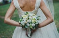 Beautiful bride in satin lace dress and veil is holding bouquet behind her back. Roses, eustoma and eucalyptus elegant flowers.