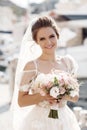 Young beautiful bride in a white elegant dress posing alone on the rocky shore of the blue ocean on a summer sunny day Royalty Free Stock Photo