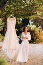 A beautiful bride stands next to a wedding dress with a Cup of tea in a boudoir outfit next to a Villa in Italy.morning of the