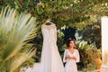 A beautiful bride stands next to a wedding dress with a Cup of tea in a boudoir outfit next to a Villa in Italy.morning of the