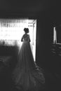 Beautiful bride style. Wedding girl stand in luxury wedding dress near window. Black and white