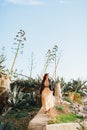 Beautiful bride in sunglasses, pastel wedding dress and leather jacket walks along the path between agaves