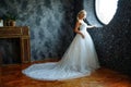 A beautiful bride in a very beautiful long dress with a train stands by the window
