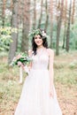 Beautiful bride walking in a coniferous forest in a wreath on her head and a luxurious wedding dress, holding rustic Royalty Free Stock Photo