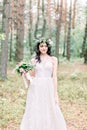 Beautiful bride walking in a coniferous forest in a wreath on her head and a luxurious wedding dress, holding rustic Royalty Free Stock Photo