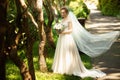 Beautiful bride walking in the park. Wedding veil disperse of wind. Beauty portrait of a bride around amazing nature