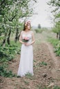 Beautiful bride in a wedding dress with bouquet and roses wreath posing in a green garden Royalty Free Stock Photo