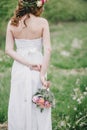 Beautiful bride in a wedding dress with bouquet and roses wreath posing in a green garden Royalty Free Stock Photo