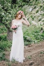 Beautiful bride in a wedding dress with bouquet and roses wreath posing in a green garden Royalty Free Stock Photo