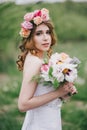 Beautiful bride in a wedding dress with bouquet and roses wreath posing in a green garden Royalty Free Stock Photo