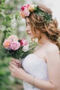 Beautiful bride in a wedding dress with bouquet and roses wreath posing in a green garden Royalty Free Stock Photo