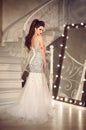 Beautiful Bride in wedding dress posing by staircase in luxurious interior. Elegant brunette woman in long gown standing by Royalty Free Stock Photo