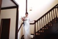 Beautiful bride in a white dress with a bouquet of flowers in her hands goes down the stairs Royalty Free Stock Photo