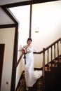 Beautiful bride in a white dress with a bouquet of flowers in her hands goes down the stairs Royalty Free Stock Photo