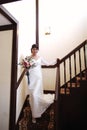 Beautiful bride in a white dress with a bouquet of flowers in her hands goes down the stairs Royalty Free Stock Photo