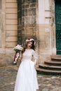 Beautiful bride in white dress with a bouquet of flowers and a wreath on the background of an old building Royalty Free Stock Photo