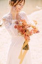 Beautiful bride in a white dress with sleeves and lace, with a yellow autumn bouquet of dried flowers and peony roses