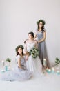 Beautiful bride in a white wedding dress holding bouquet and sitting on the vintage chair with bridesmaids in blue grey